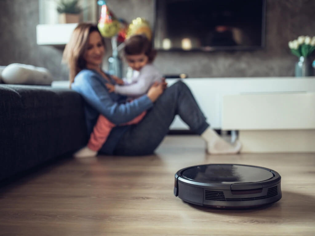 A woman and her child sitting next to a mini robot vacuum